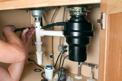 Plumber repairing a garbage disposal beneath a kitchen sink in Palm City