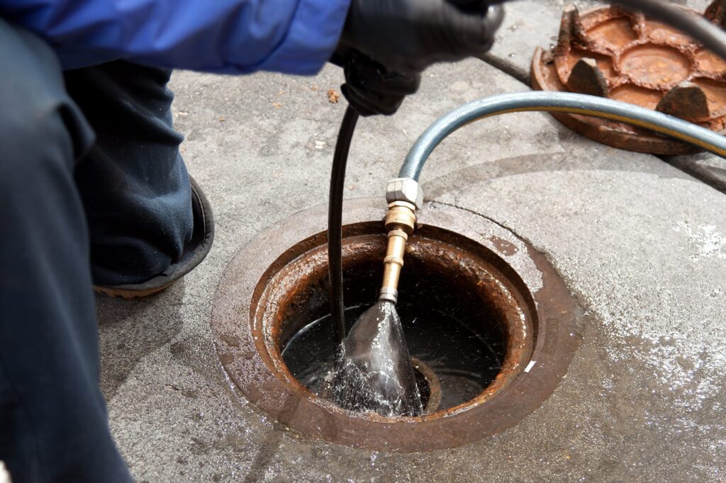 Plumber hydro jetting a sewer line through a manhole in Palm City