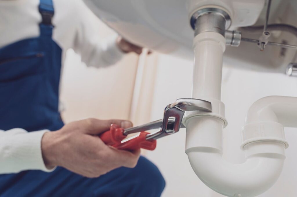 Plumber repairing a white drain pipe beneath a sink in Palm City