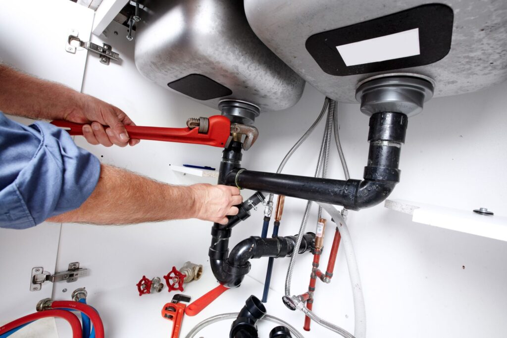 Plumber repairing drain pipes beneath a kitchen sink in Palm City